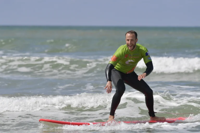 Adulte souriant debout sur la planche de surf planche de surf rouge cours de surf de surf Côte Sauvage – ESCS La Palmyre Côte Sauvage