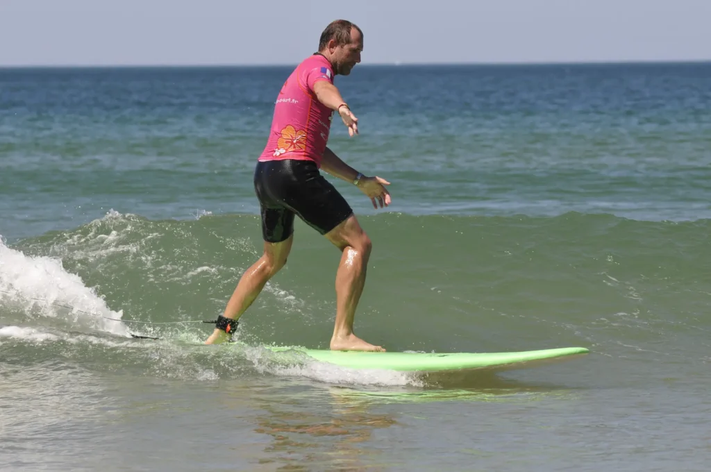 Moniteur de surf ESCS lycra rose en glisse sur une vague Côte Sauvage – ESCS La Palmyre Côte Sauvage
